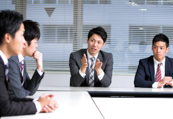 写真：スーツ姿の男性4人がL字型のテーブルについて話をしている